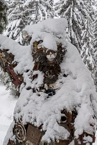 Standing bear sculpture made of gears and scrap metal, covered in snow