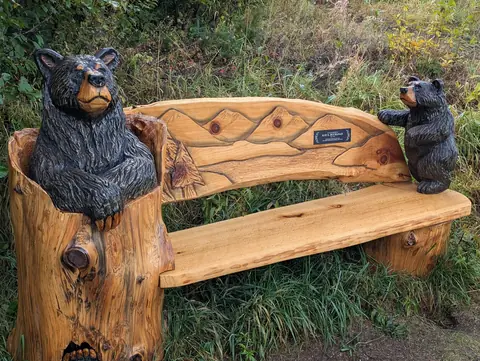 Rustic log bench with a carved bear seated at one end and a small cub perched on the other