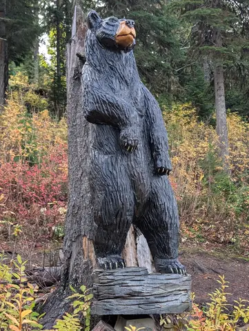 Chainsaw-carved wooden black bear standing upright on a log base