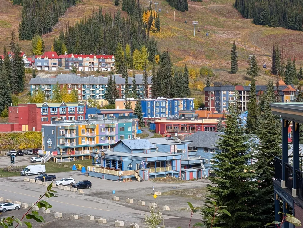 Brightly painted red, blue, yellow and teal village buildings below a ski run in fall