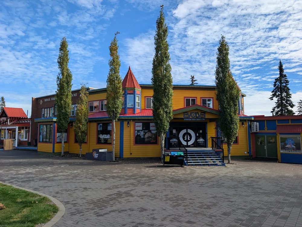 Brick-paved village square with tall poplars and a yellow and red building