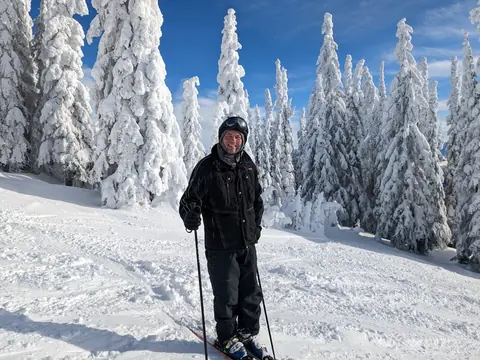 Skier standing among snow-laden trees on a groomed run