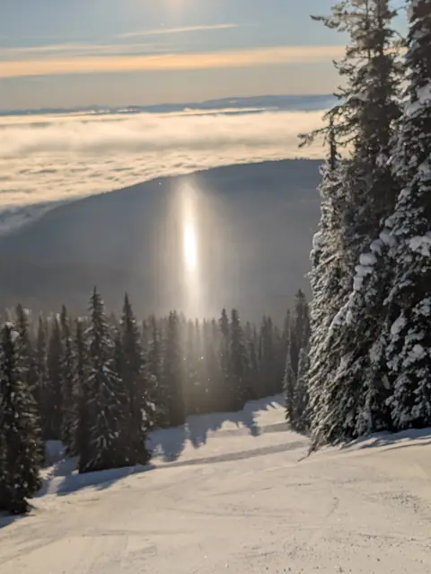 Sun pillar of light above a groomed ski run and snowy trees, January 26, 2025, morning