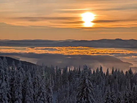 Low winter sun above glowing valley cloud and snow-covered forest, December 9, 2024