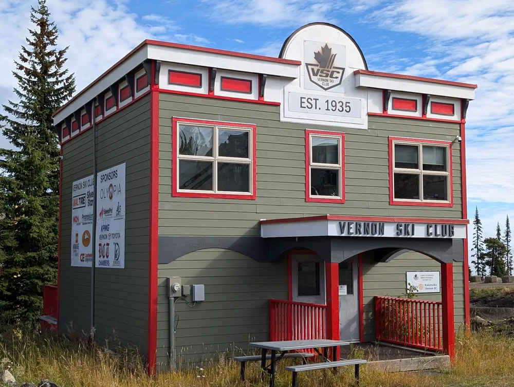 Grey clapboard village building with a round Vernon Ski Club crest marked Est. 1935